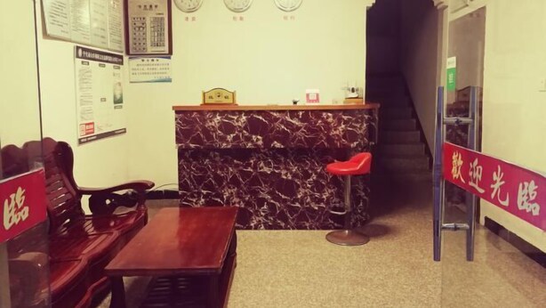 Un espace d’accueil avec un comptoir en marbre, des chaises en bois, une petite table et un tabouret rouge. Il y a des horloges au mur et une enseigne avec des caractères chinois.