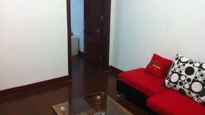 Un canapé rouge avec un coussin à motifs noir et blanc, une table basse en verre et un plancher en bois.