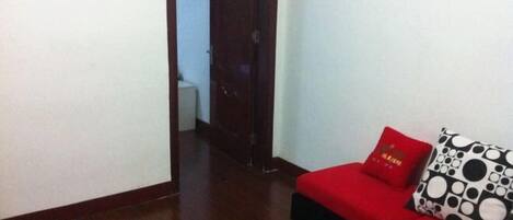 Un sofá rojo con un cojín estampado en blanco y negro, una mesa de centro de vidrio y un piso de madera.
