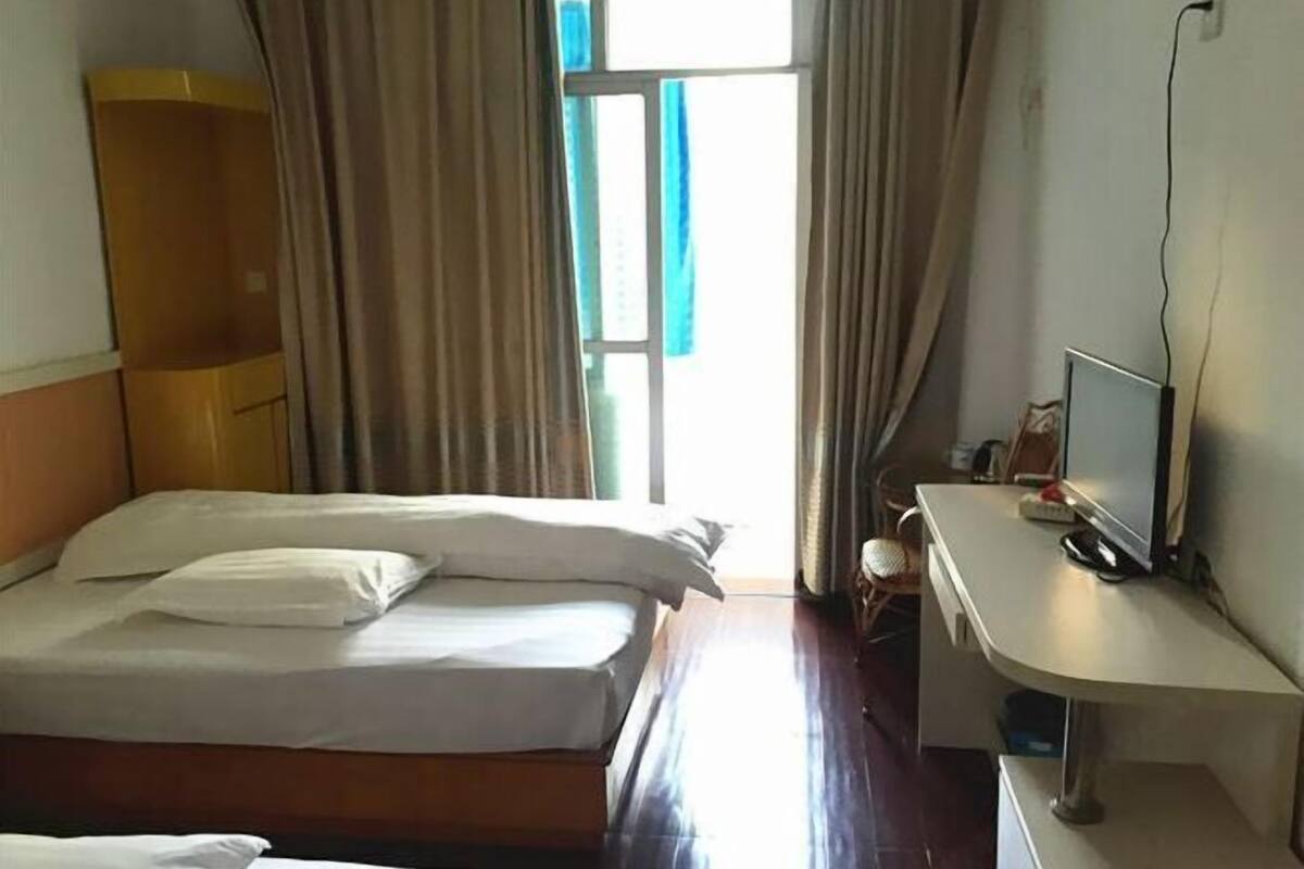 Ein Hotelzimmer mit einem Bett, einem Schreibtisch mit Computer und einem Fenster mit Vorhängen.