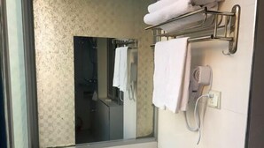 Une salle de bain avec un grand miroir, un porte-serviettes avec des serviettes, un lavabo avec un robinet et un sèche-cheveux branché.