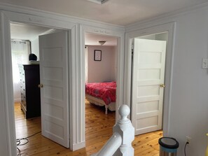 A room with a bed, a dresser, and a door leading to another room. - Traditional Newfoundland House (Fermeuse)
