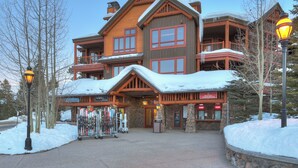 Un grand chalet doté de nombreux balcons et d’une façade en pierre, avec un espace de location de matériel de ski situé à l’avant.