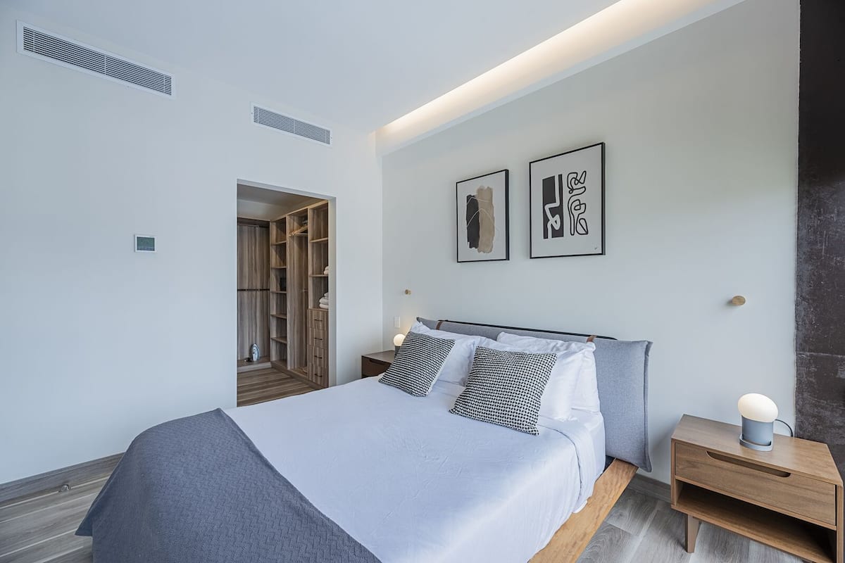 Un dormitorio moderno con cama, mesitas de noche, armario y una obra de arte en la pared.