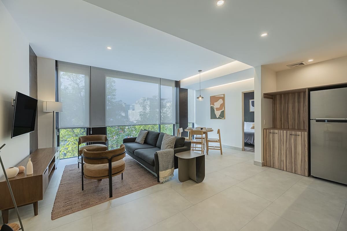 Uma sala de estar moderna com sofá, cadeiras, mesa de jantar e área de cozinha com geladeira.