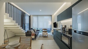 Een moderne keuken met een vast eiland, een eethoek met een houten tafel en stoelen, een bank en een trap met een leuning.