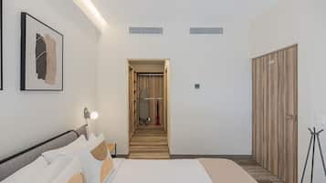 Une chambre d’hôtel comprenant un lit, une table de chevet, une lampe, un tableau encadré, une armoire et un couloir menant à la salle de bain.