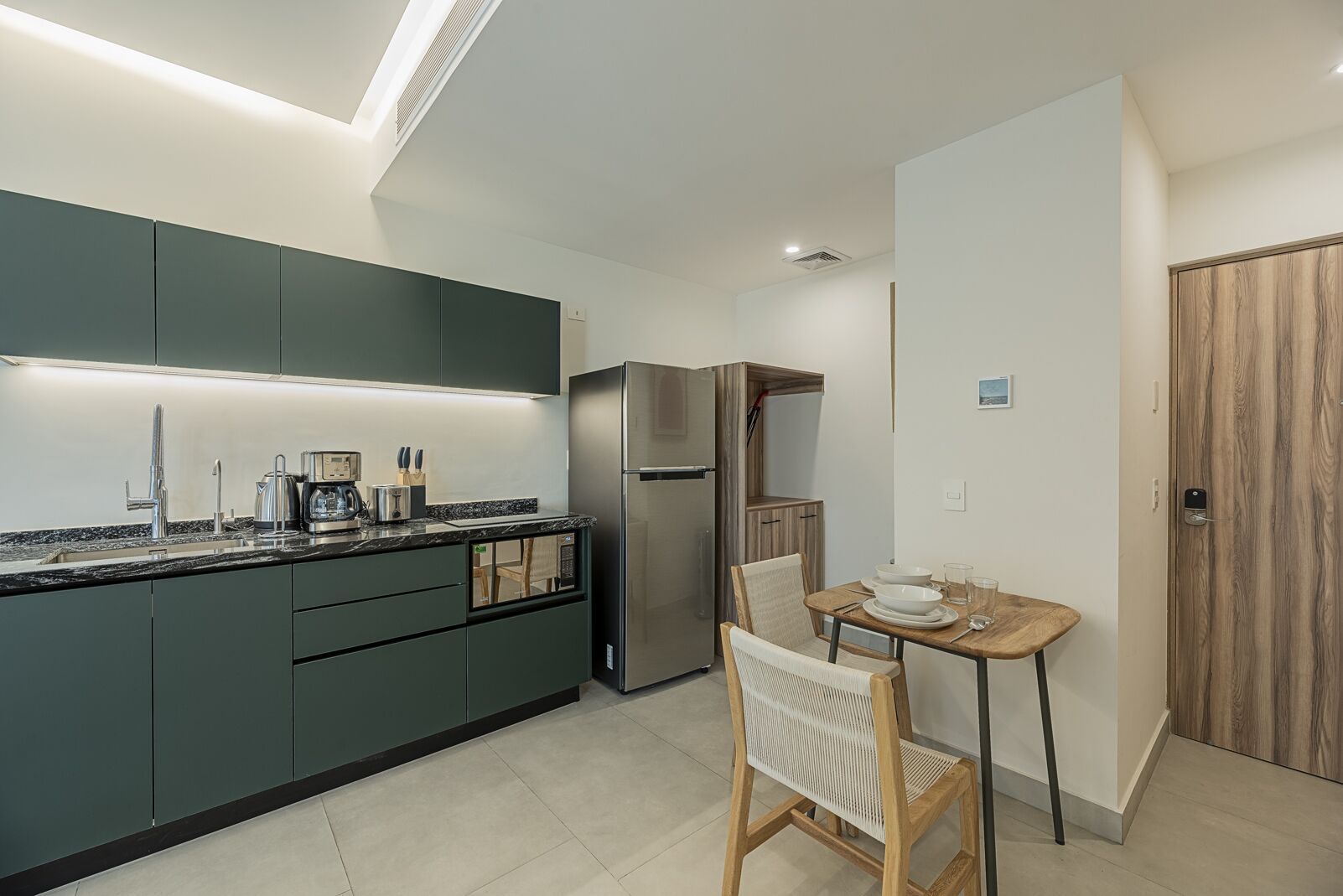 Une cuisine moderne avec des meubles de couleur sombre, un réfrigérateur en acier inoxydable et un coin repas comprenant une table et des chaises en bois.