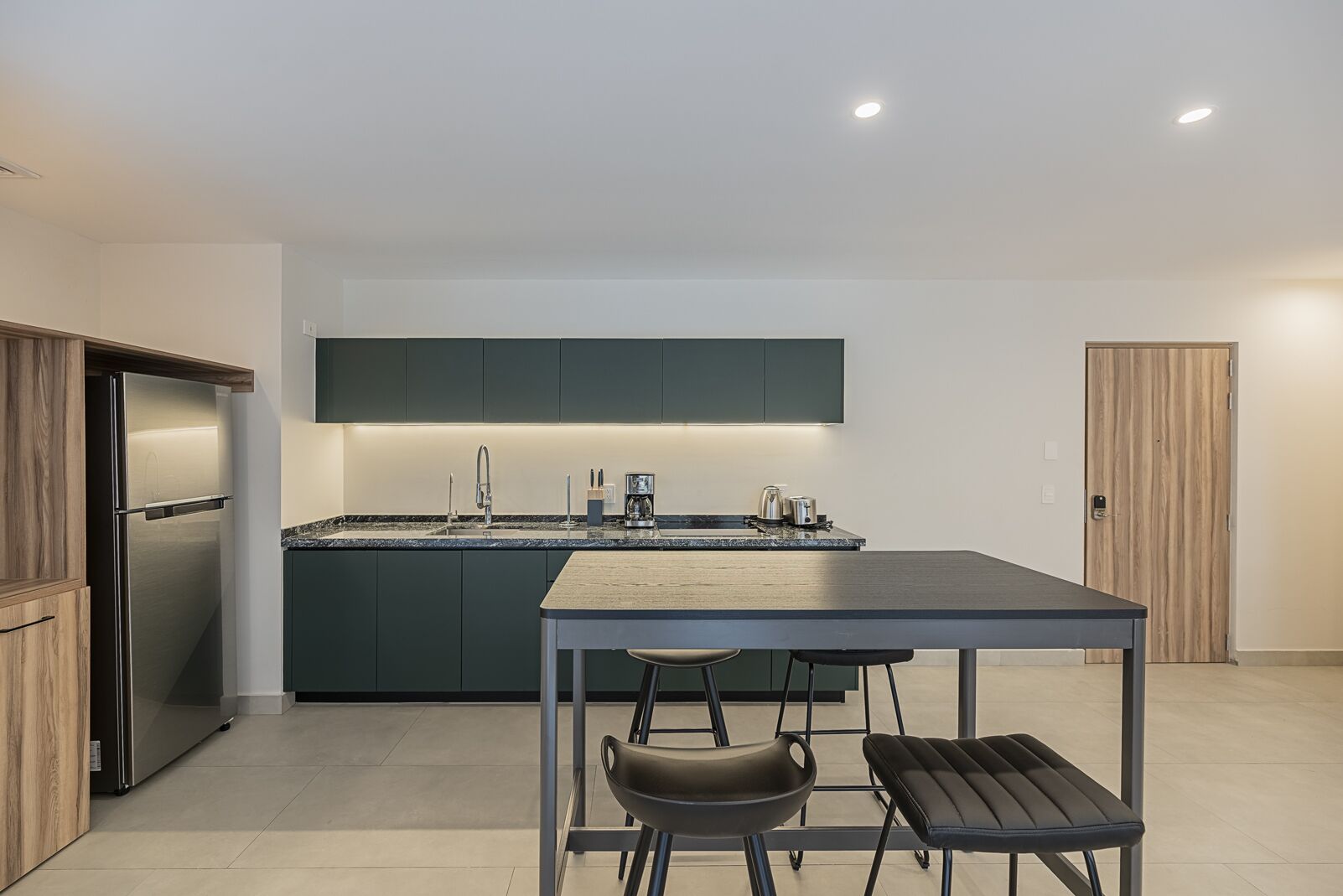 A modern kitchen with a central island, dark cabinetry, stainless steel appliances, and a minimalist dining area with two stools.