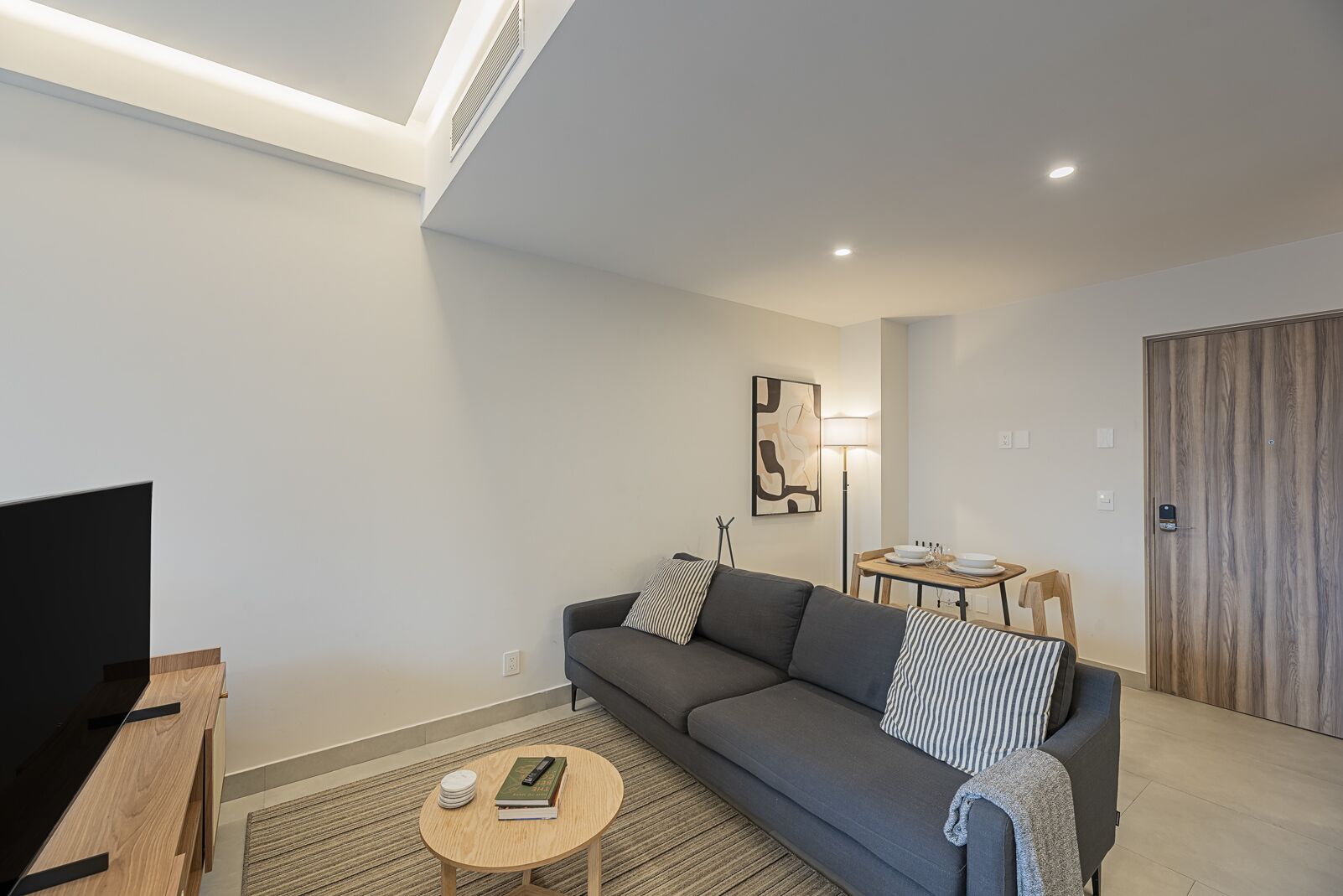Una sala de estar moderna con un sofá gris, una mesa de centro, un televisor y un comedor con mesa y sillas.