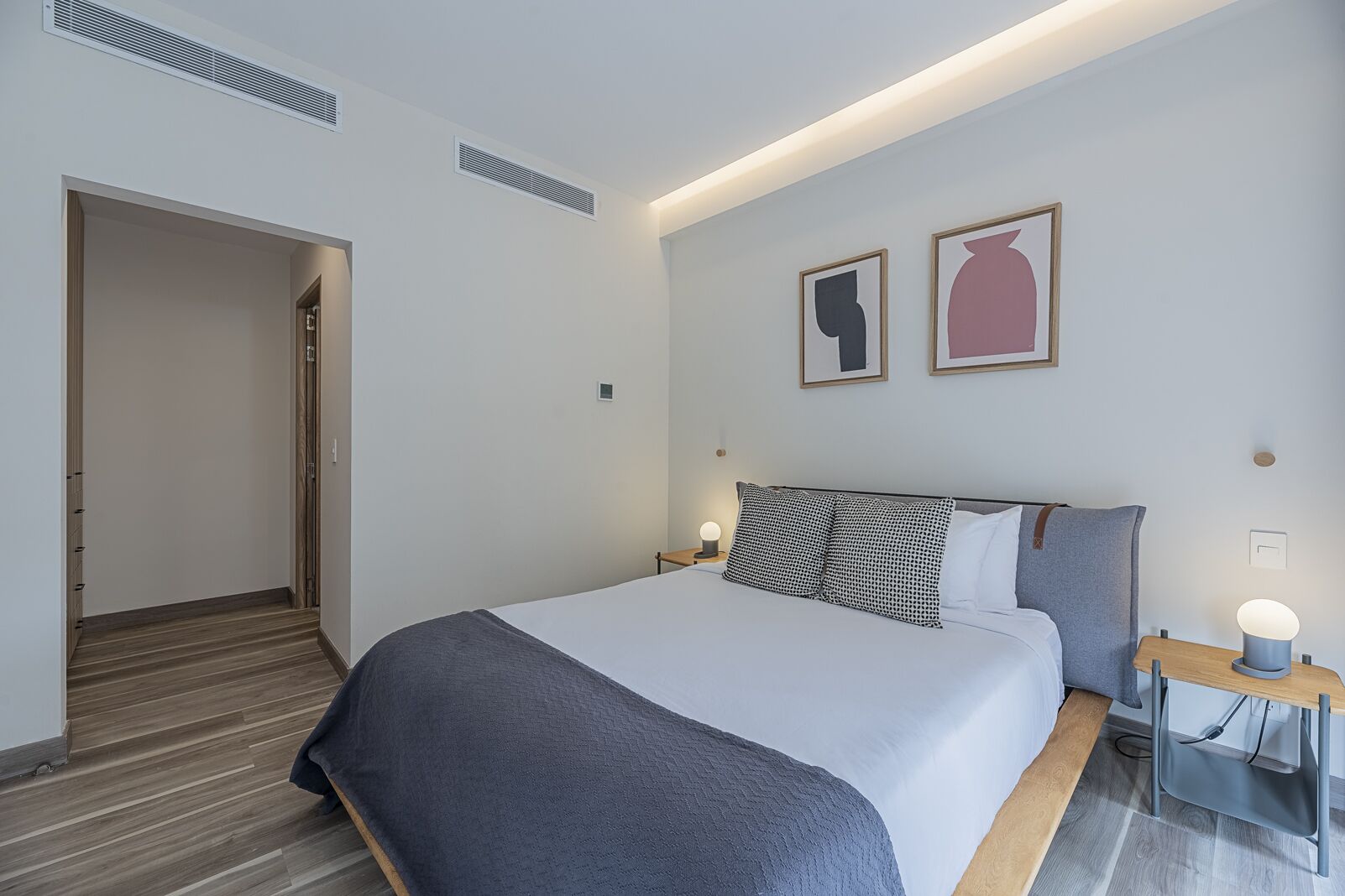 Ein modernes Hotelzimmer mit einem großen Bett, einem Nachttisch mit Lampe sowie zwei gerahmten Kunstwerken an der Wand.