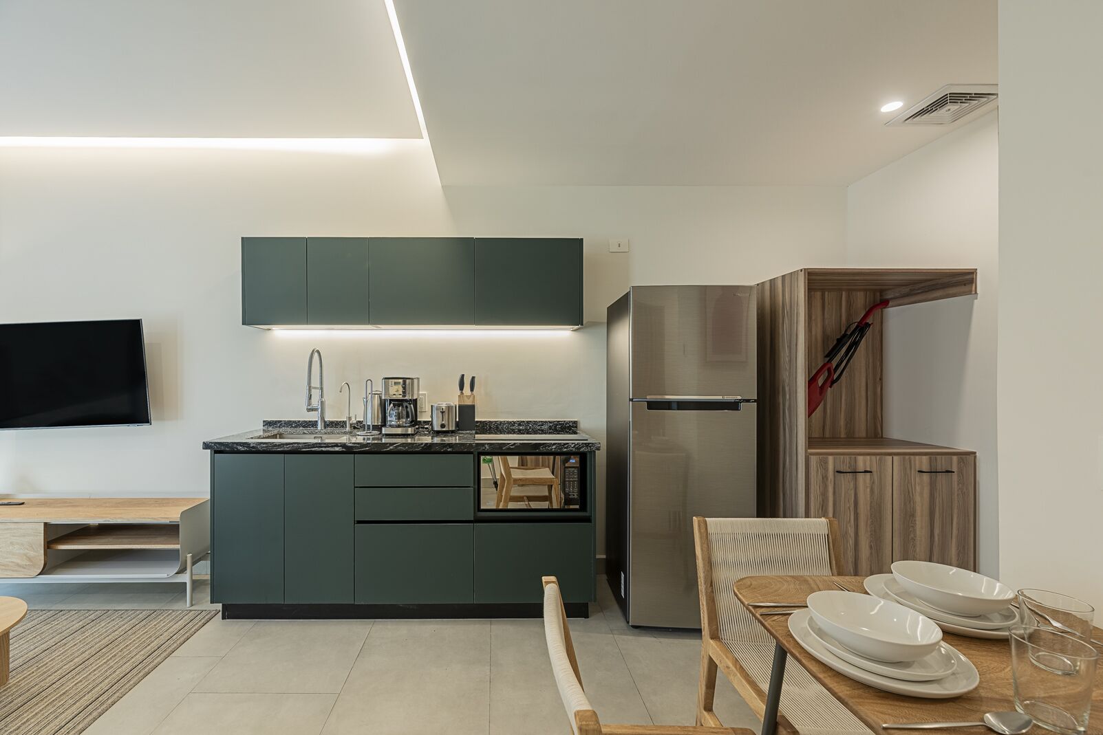Una cocina moderna con refrigerador integrado, cafetera y televisor de pantalla plana montado en la pared.