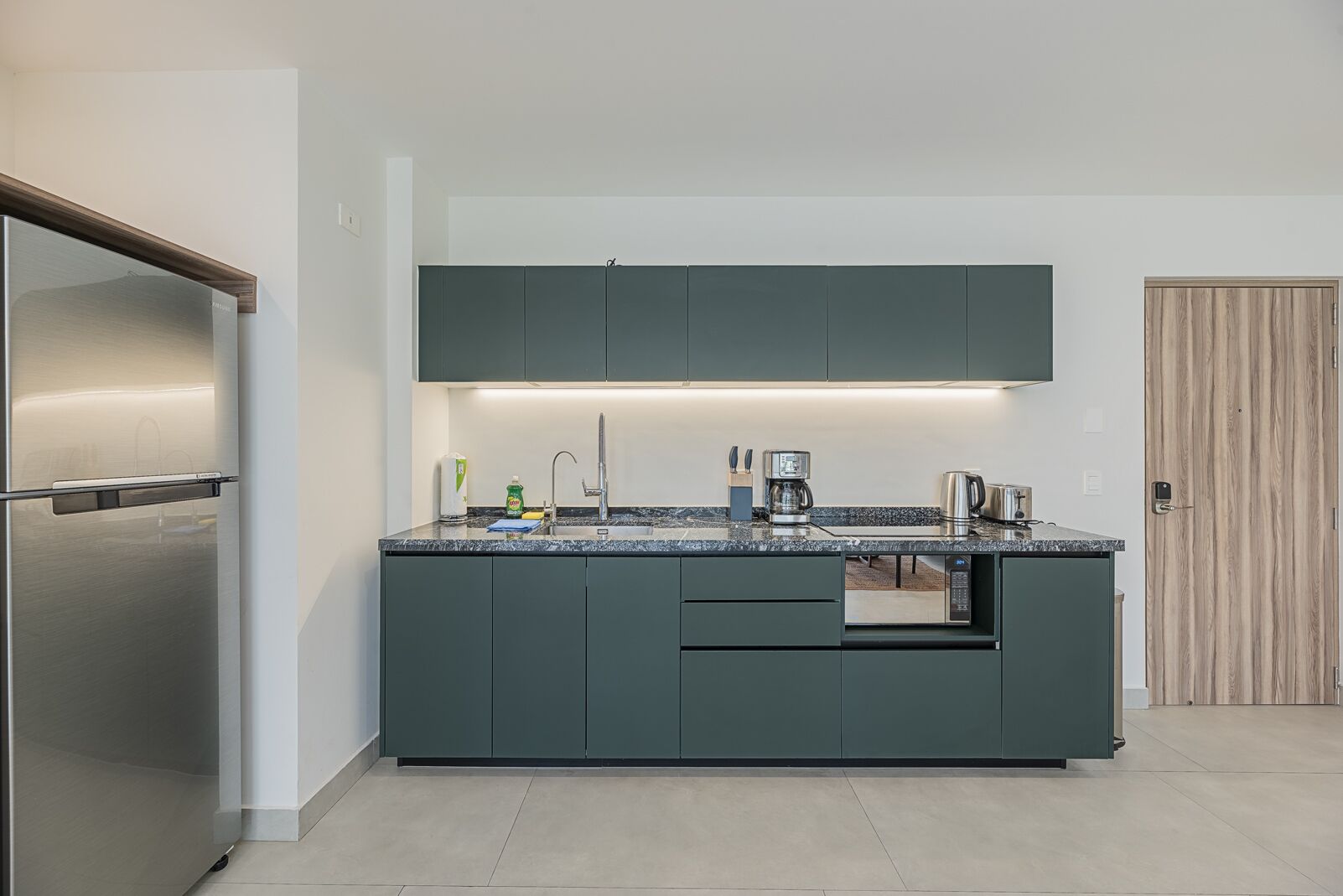 A modern kitchen with dark cabinets, a stainless steel refrigerator, and a built-in coffee maker.