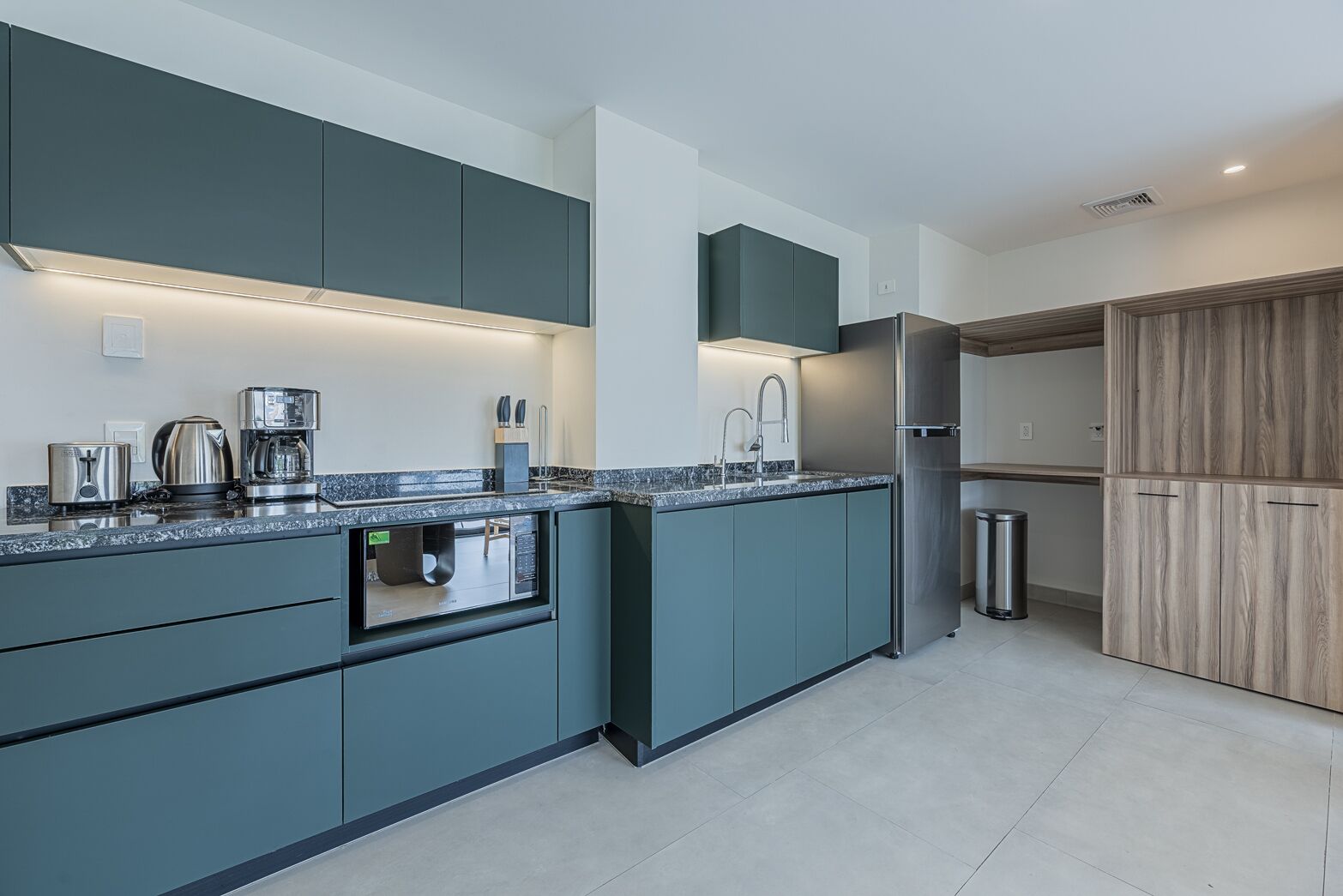 A modern kitchen with dark teal cabinetry, a stainless steel refrigerator, and a built-in oven.