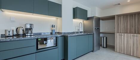 A modern kitchen with dark teal cabinetry, a stainless steel refrigerator, and a built-in oven.