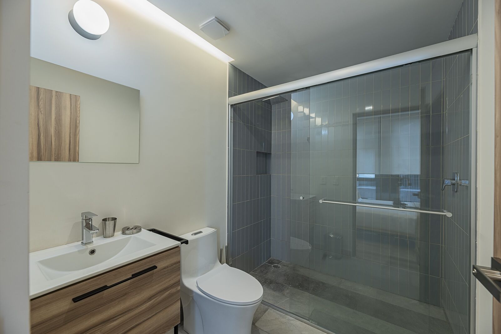 A modern bathroom with a glass shower enclosure, a wooden vanity, and a white sink.