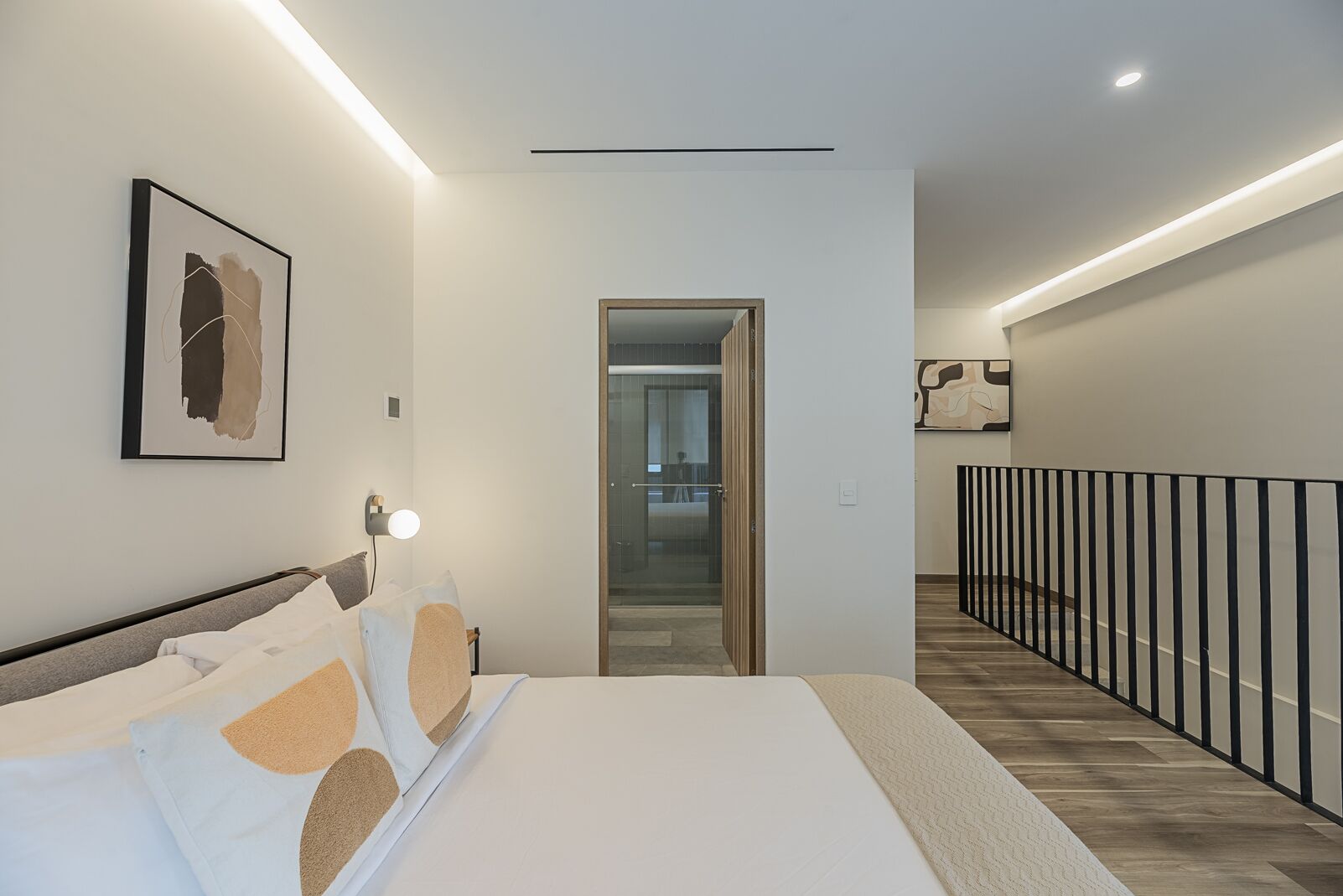 Ein modernes Schlafzimmer mit einem großen Bett, einem Nachttisch, einer Wandleuchte und einem gerahmten abstrakten Kunstwerk.