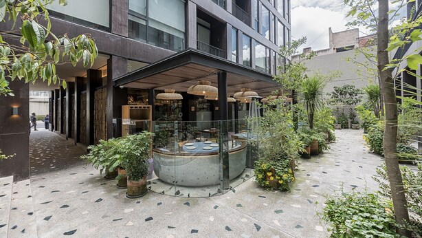 Een modern gebouw met een overdekt terras, omringd door potplanten en bomen.