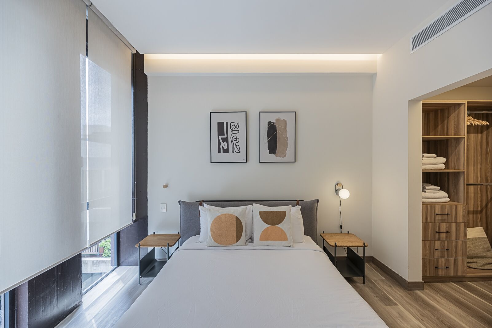A modern bedroom with a large bed, bedside tables, a wardrobe, and artwork on the wall.