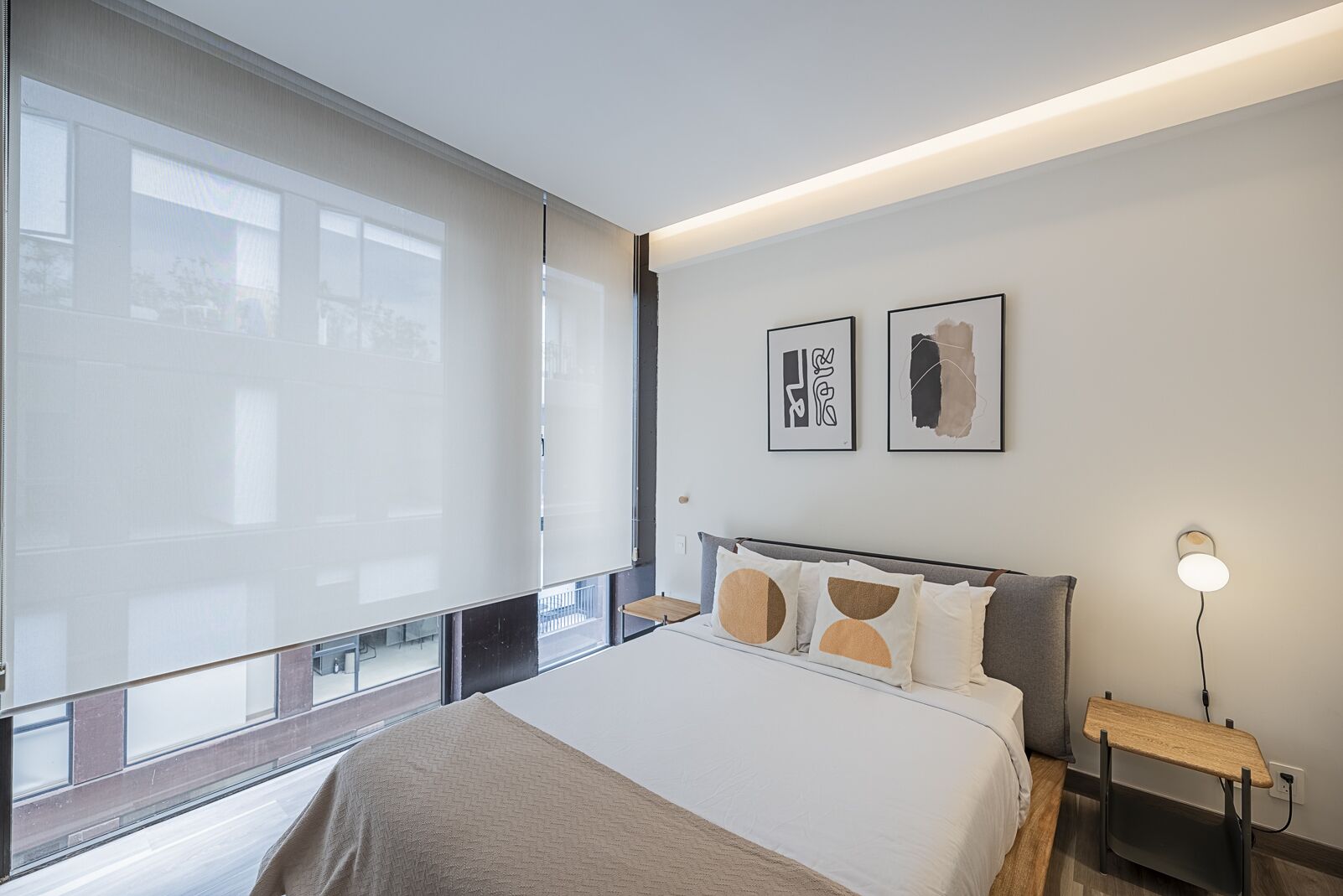 A modern hotel room with a large bed, a bedside table with a lamp, and two framed artworks on the wall.