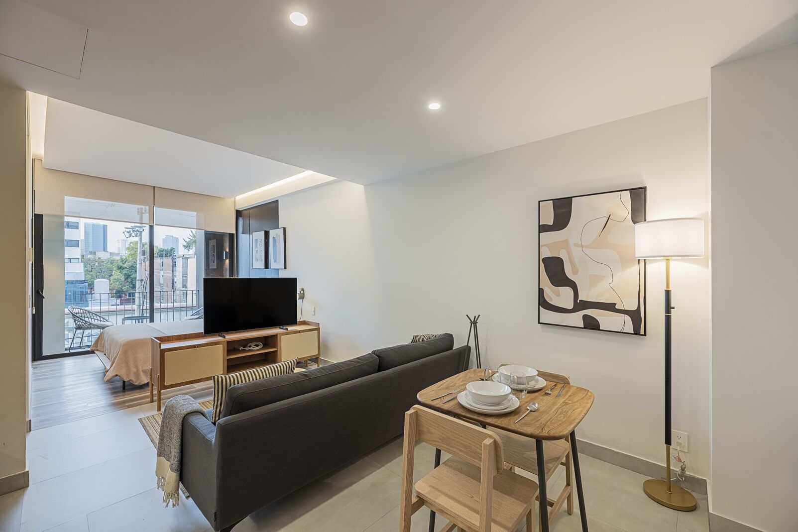 A modern living room with a sofa, TV, and dining table with plates and cutlery.