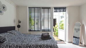 Un dormitorio con colcha de estampado de cebra, un espejo de pie y vistas a un jardín a través de una puerta corrediza.