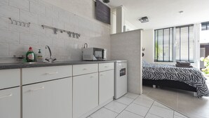 Una cocina moderna con armarios blancos, un microondas y un fregadero. En la habitación contigua hay una cama con cubrecama estampado con cebra.