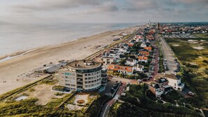 Vista aérea de un pueblo costero con una playa, edificios residenciales y un gran hotel de diseño circular.
