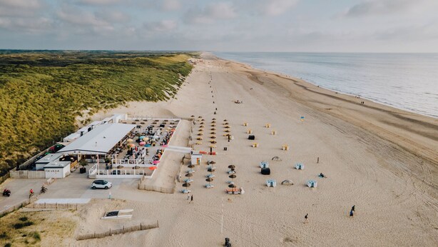Un hotel frente a la playa con zona de comedor, sombrillas de playa y una playa de arena.