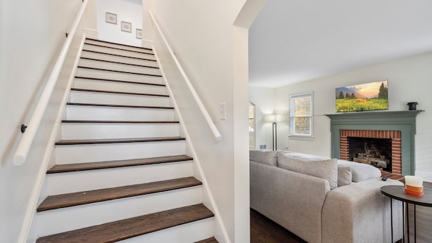 A staircase with wooden steps and white railings, a gray sofa, a fireplace, and a painting on the wall. - Beautiful, Spacious 4 Bedroom Home one Block from High Point University (High Point)