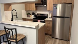 A modern kitchen with wooden cabinets, a stainless steel refrigerator, a microwave, a stove, and a sink. - Remodeled 3-bedroom condo in Marina walking distance to beach; STR25-000040 (Marina)