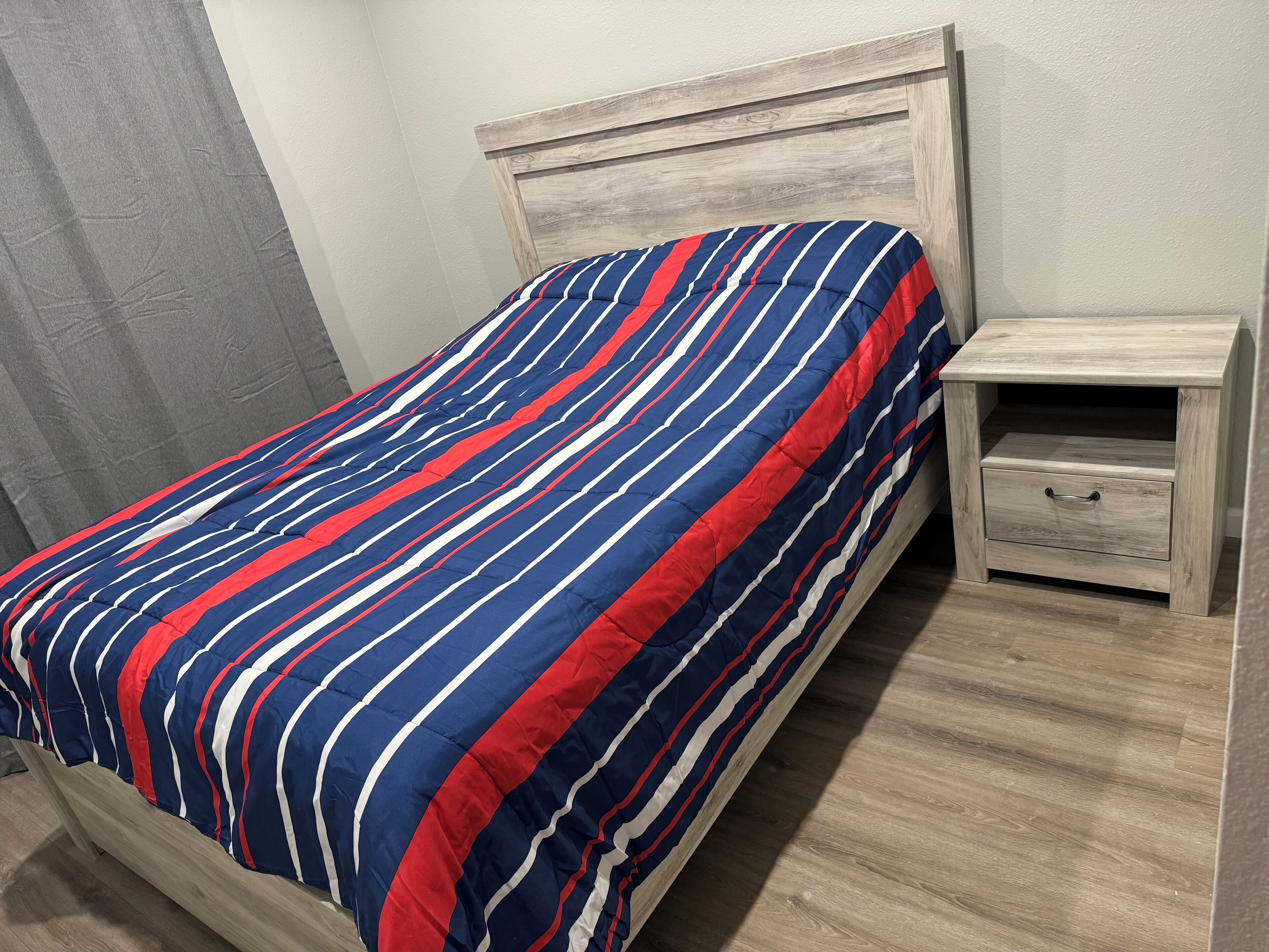 Ein Bett mit gestreifter Bettdecke, einem Holzkopfbrett und einem Nachttisch mit Schublade.
