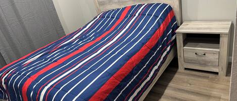 Ein Bett mit gestreifter Bettdecke, einem Holzkopfbrett und einem Nachttisch mit Schublade.