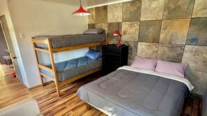 Ein Schlafzimmer mit einem Etagenbett, einem Einzelbett, einem Nachttisch mit Lampe und Holzboden.