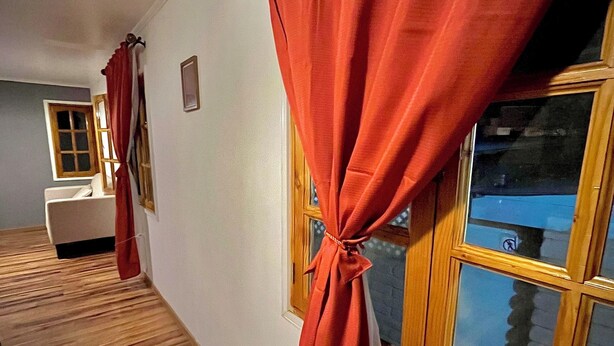 Ein Flur mit Holzboden, einem Fenster mit Aussicht und einem roten Vorhang, der am unteren Ende gebunden ist.