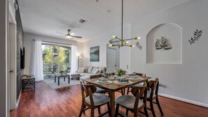 A dining area with a wooden table set for four, surrounded by chairs. There is a ceiling fan, a chandelier, and a wall-mounted sailboat decoration.