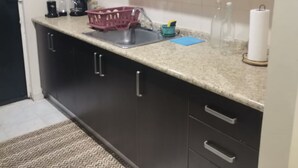 Eine Küche mit dunklen Schränken, einer Granit-Arbeitsplatte, einer Kaffeemaschine, einem Korb und einer Küchenpapierrolle.