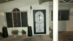 Ein Gebäudeeingang mit einer schwarzen Tür, einem Fenster mit Gitterstäben und Blumentöpfen.