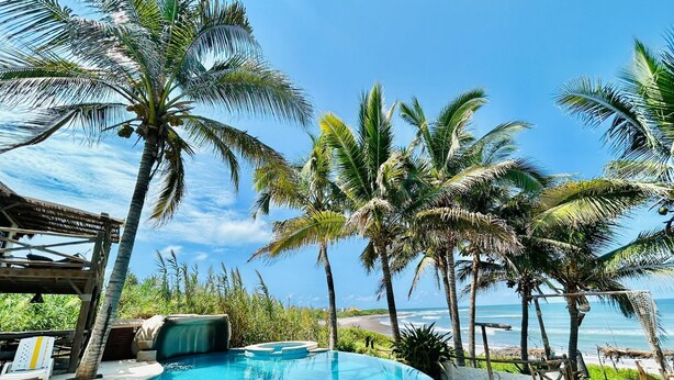 Un espace aménagé au bord de la piscine, comprenant un jacuzzi, des chaises longues et des palmiers.