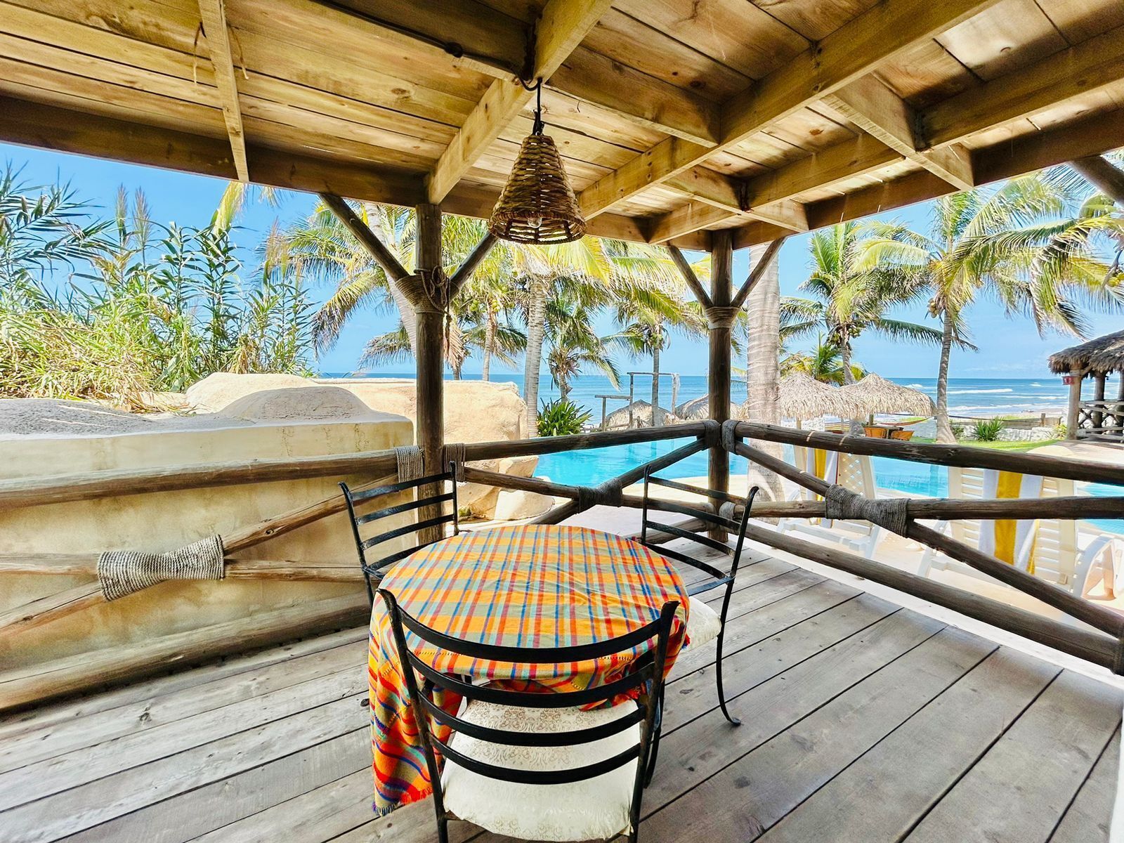 A wooden deck with a table and chairs, overlooking a pool and palm trees.