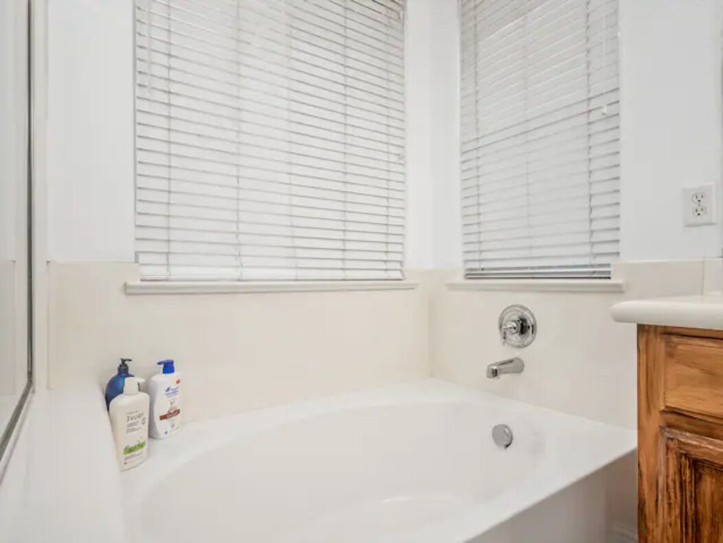 A bathroom with a bathtub, two bottles of toiletries, and a wooden cabinet.