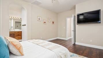 A bedroom with a bed, a ceiling fan, a TV, and a door leading to another room.