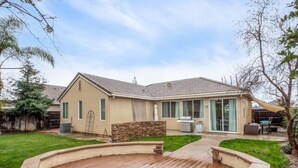 A house with a backyard deck, a stone wall, and a grassy lawn. - Fresno House - BBQ, Fire Pit, 3 Bed, 2 Bath & 2 Car Garage! (Fresno)