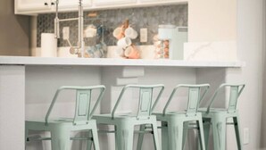 A kitchen with a white countertop, a stainless steel faucet, and a tiled backsplash. There are four green bar stools aligned against the wall. - Fresno House - BBQ, Fire Pit, 3 Bed, 2 Bath & 2 Car Garage! (Fresno)