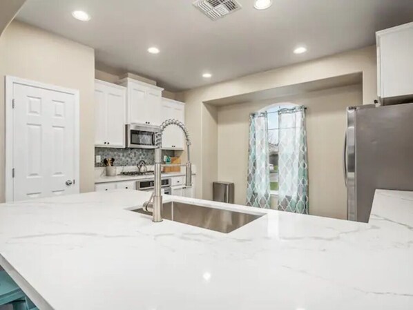 A modern kitchen with white cabinets, a stainless steel refrigerator, and a marble countertop. - Fresno House - BBQ, Fire Pit, 3 Bed, 2 Bath & 2 Car Garage! (Fresno)
