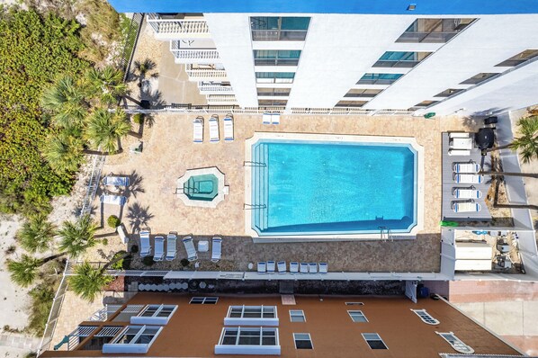 Vista aérea de un hotel con piscina, tumbonas y una zona cubierta con vistas a la piscina.
