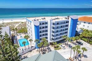 A multi-story hotel with a pool, beach view, and parking area.