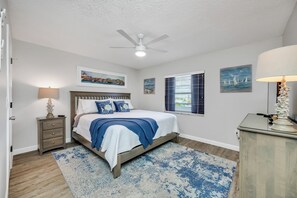 A bedroom with a bed, a nightstand, a ceiling fan, and artwork on the walls.