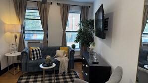 Ein modernes Wohnzimmer mit einer Couch, einem kleinen runden Tisch, einem schwarzen Schrank und einer großen Pflanze.