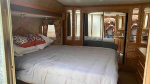 A bedroom with a large bed, wooden wardrobe, and a mirror. - Lake shore queen bed trailer, tiki torches, & tent space for extra guest (Clifton)